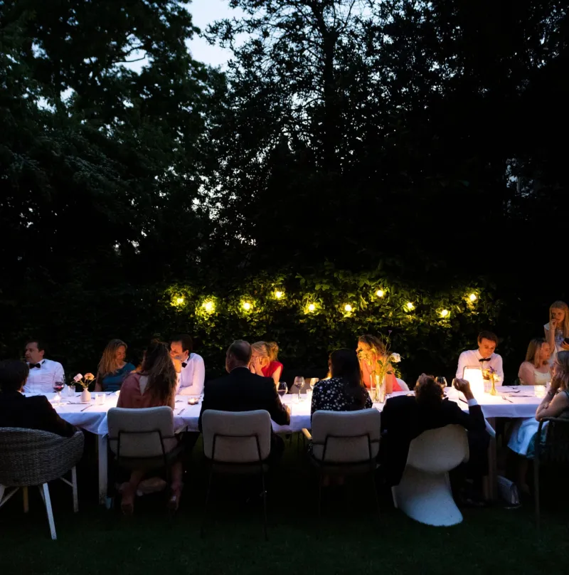 Long dinner table in the garden with string lights at dusk