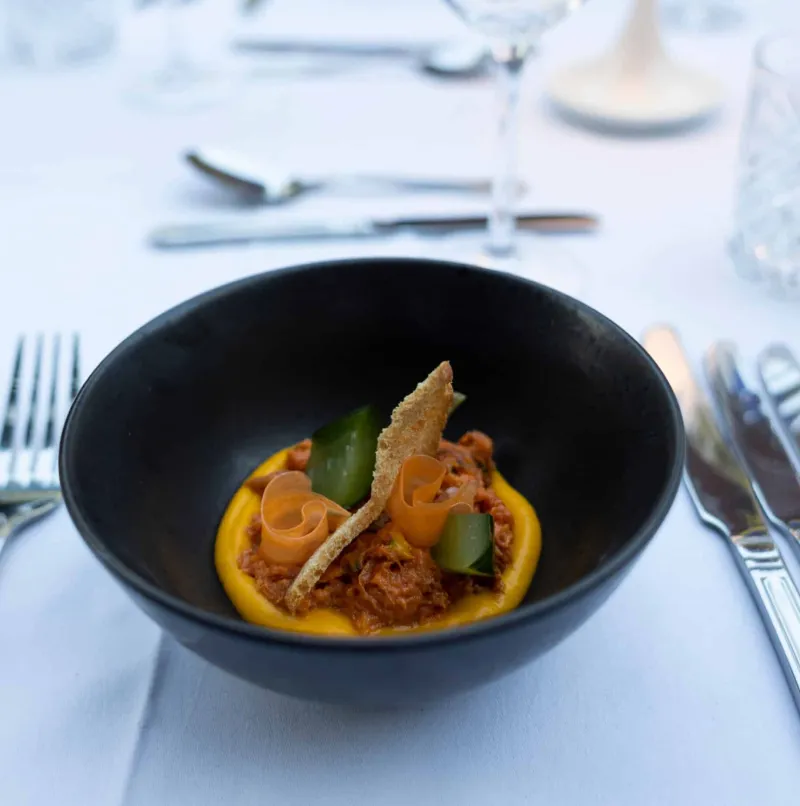 Dish with carrot purée and garnish in a black bowl